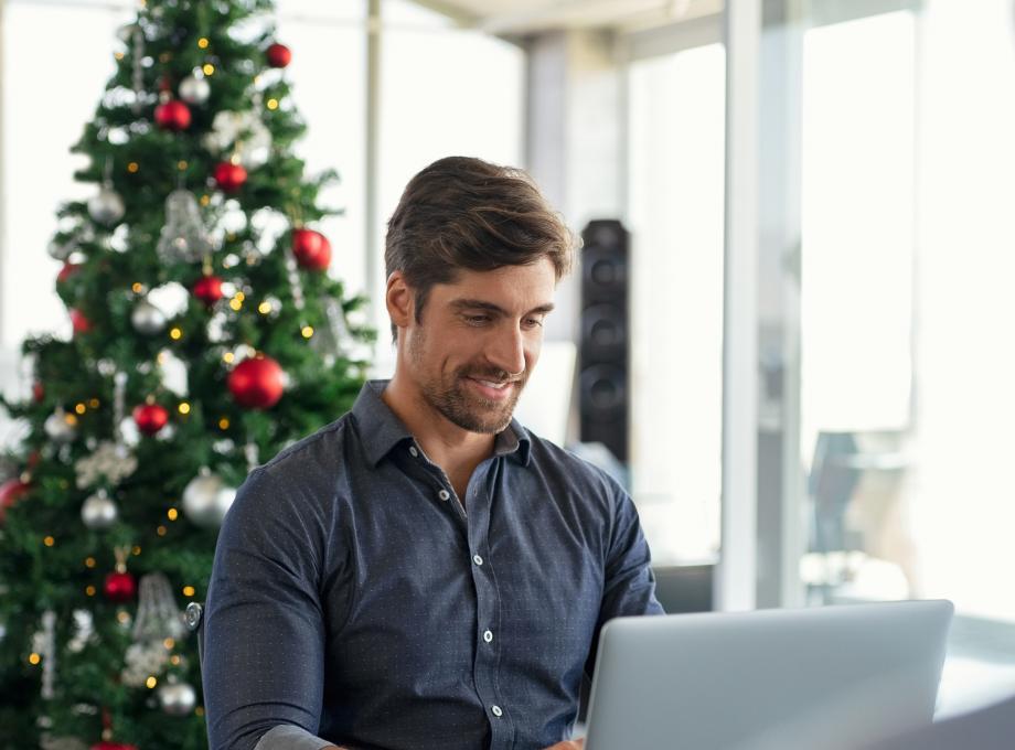 Homme travaillant sur son ordinateur avec un sapin décoratif en fond