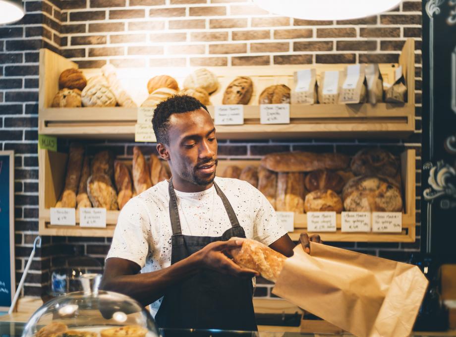 Jeune boulanger emballant une baguette de pain dans un sac en papier au comptoir de son commerce