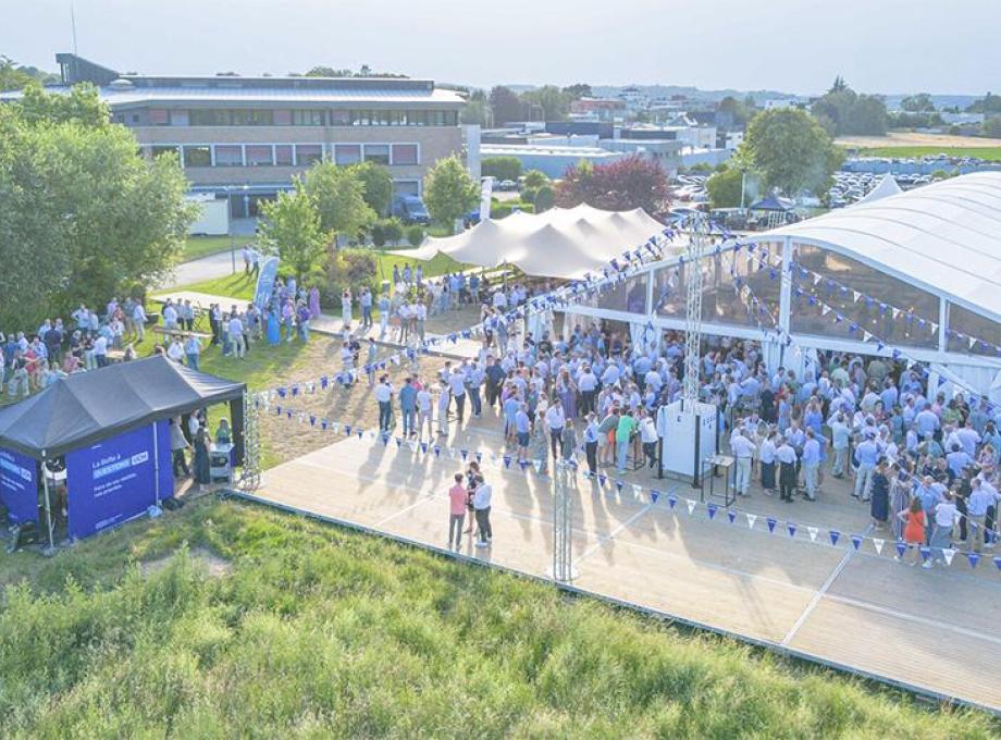 Une grande foule se rassemble sous un chapiteau lors d'un événement extérieur.