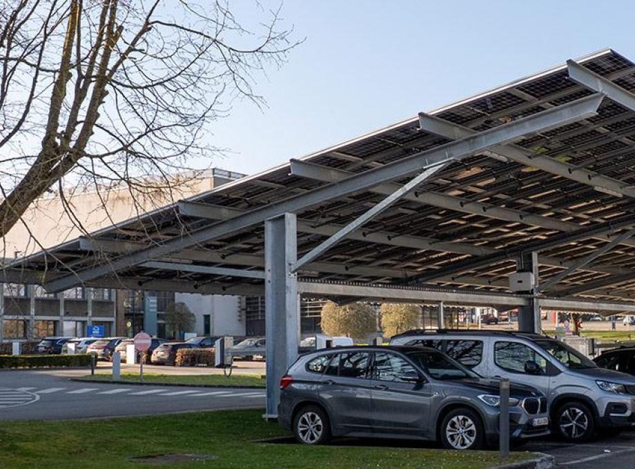 Aire de stationnement sous une structure de panneaux solaires, voitures garées.