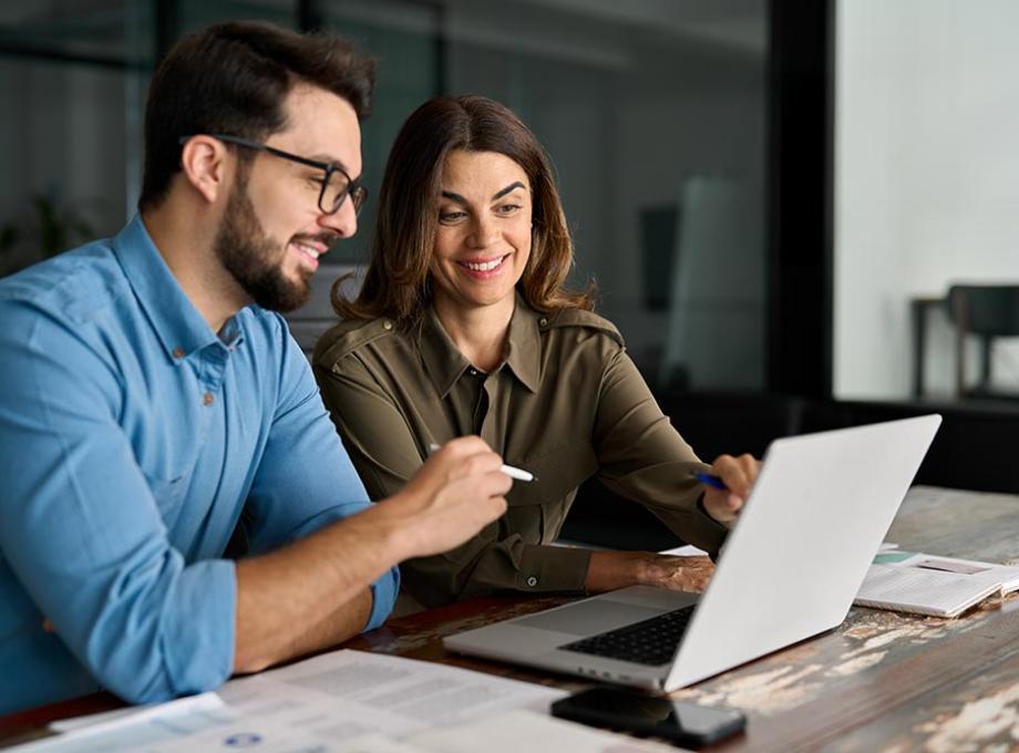 Un homme et une femme souriant, collaborant devant un ordinateur portable.