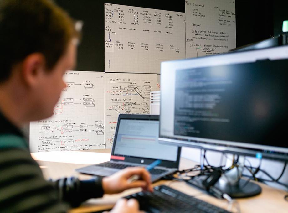 Un homme travaillant sur un ordinateur portable avec un écran de code en arrière-plan.